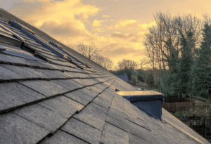 Roofing shingles on a sloped roof with a sunset backdrop, emphasizing the importance of professional roof inspections for safety and building code compliance.